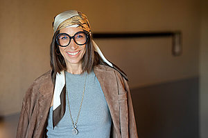 Frau mit langen dunklen Haaren, dick umrandeter Brille und stylischem Kopftuch. 
