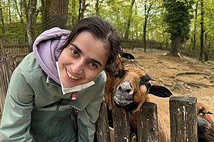 Junge Frau lächelt neben einem Zootier in die Kamera