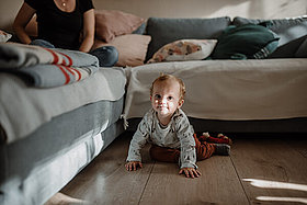Ein etwa einjähriger Junge krabbelt vor einem Sofa. 