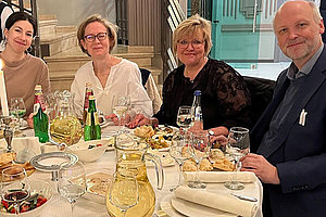 Drei Frauen und ein Mann an einem reich gedeckten Tisch mit Servietten