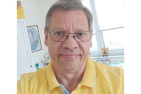 Porträt von Thomas: Mann um die 60 Jahre alt, trägt ein gelbes Polo-Shirt, im Hintergrund sieht man ein Fenster. 