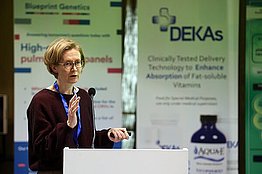 Frau mit kinnlangen Haaren beim Vortrag auf einer Konferenz.