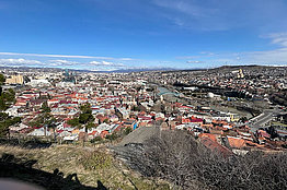Blick auf eine Stadt von einem Hügel aus, es scheint eher Winter zu sein, der Himmel ist blau. 
