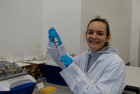 Dr. Suki Albers-Fomenko im Labor. Sie trägt einen Laborkittel und hält eine Pipette in der Hand. Foto: Mukoviszidose e.V.
