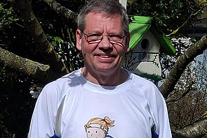 Mann - um die 60 - mit weißem T-Shirt schaut in die Kamera