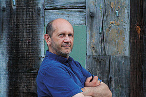 Porträt eines Mannes mittleren Alters mit vor der Brust verschränkten Armen. Er trägt ein blaues Poloshirt. 