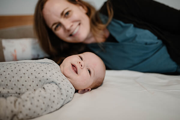 Ein lachendes Baby liegt vor seiner lachenden Mutter. 