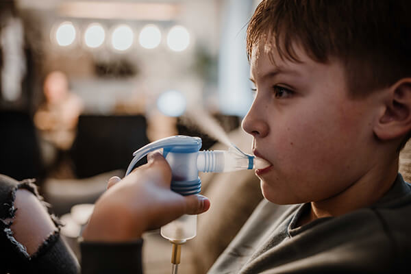 Conner inhaliert Ein elfjähriger Junge inhaliert mit einem Feuchtinhalator, man sieht Dampf aufsteigen.