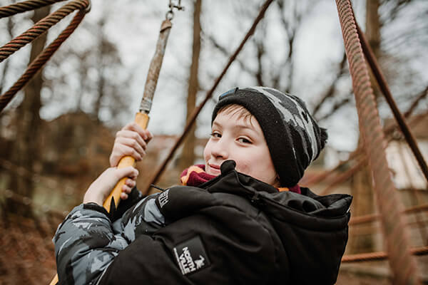 Conner auf dem Spielplatz Junge in Winterkleidung auf dem Spielplatz, er scheint auf einer Schaukel oder einem ähnlichen Spielgerät zu hängen.