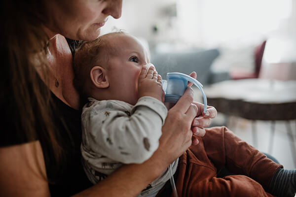 Emil inhaliert Ein Baby sitzt auf dem Schoß der Mutter und inhaliert mit einem Feuchtinhalator.