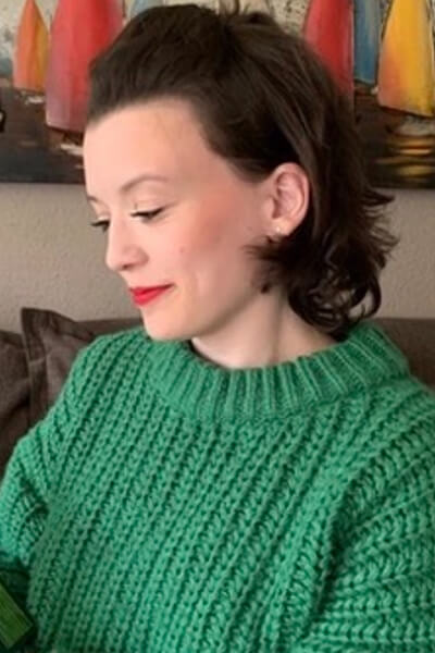 Porträt von Franziska: Sie hat kinnlange braune gelockte Haare und trägt einen grünen Strickpullover. 