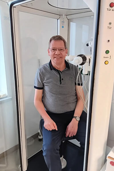 Mann sitzt in einer medizinischen Kabine, das ist ein Gerät für die Lungenfunktionsmessung. 