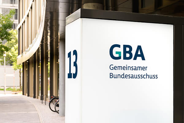 Großes Gebäude, im Mittelpunkt des Bildes ist aber ein Schild, auf dem "Gemeinsamer Bundesausschuss" zu lesen ist.